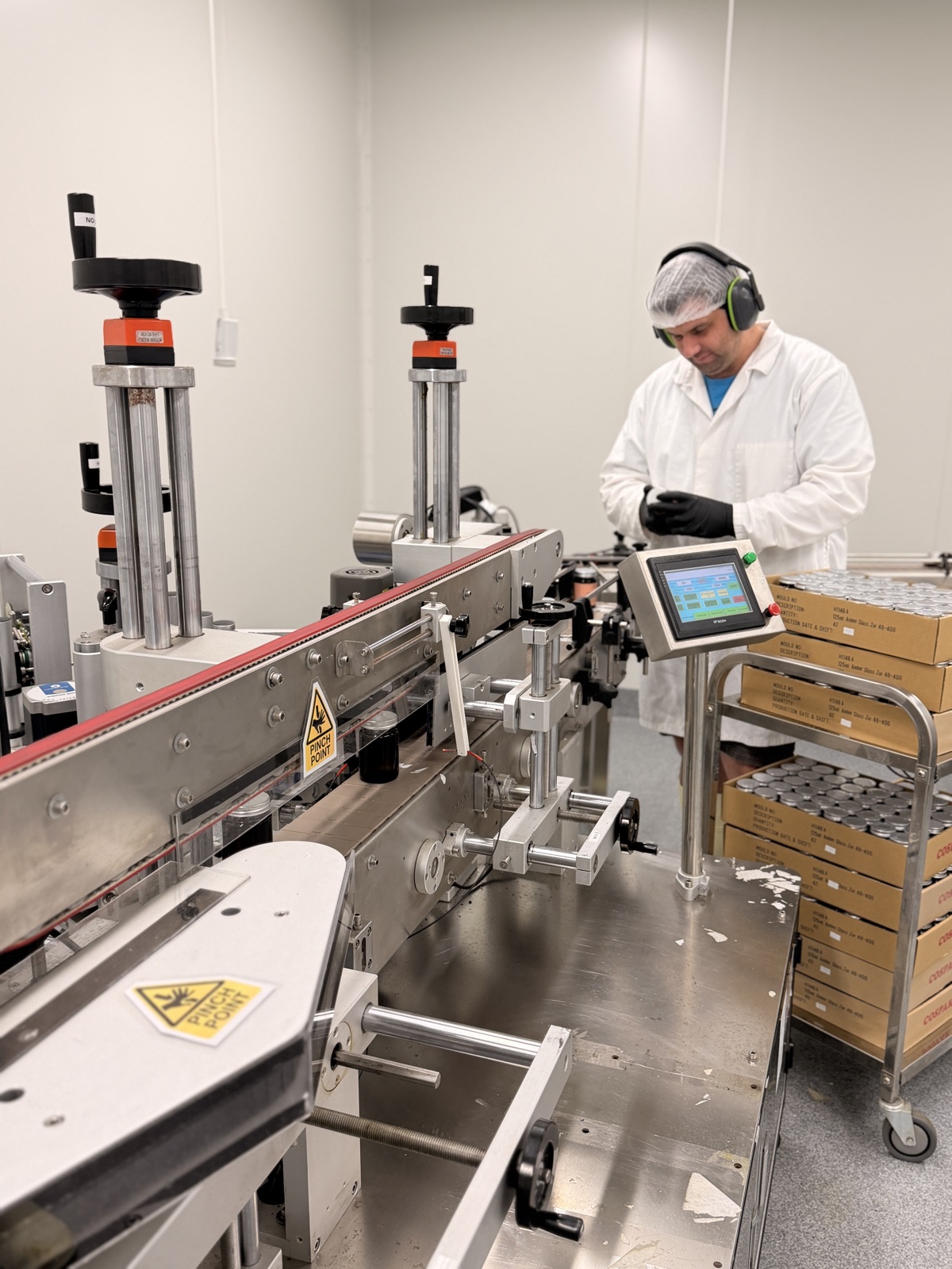 Inside the Koru facility: a team member in a hairnet and white coat working at the labelling line, with packed batches stacked beside him