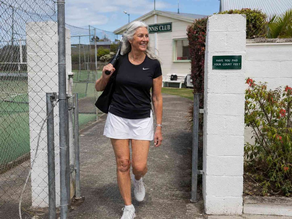 A woman walking out of the tennis club gate with her racquet over her shoulder